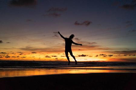 日落时在海边的人。 人在夕阳的背景下跳跃。