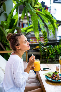 一位美丽的女人在时尚的咖啡馆里吃早餐，健康的早餐，水果，新鲜榨出的果汁，热带地区。