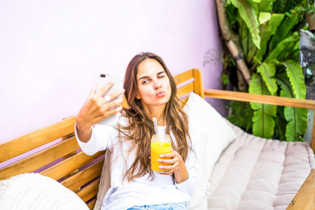 咖啡馆里的一个漂亮女人在智能手机上自拍，喝着新鲜的果汁。