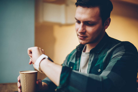 年轻男性在看智能手表触摸屏时,会收到关于拿着咖啡杯的新信息的通知