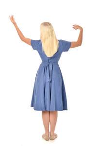穿蓝色连衣裙的金发女孩的全长肖像。 站姿背对着相机。 孤立在白色工作室背景上。
