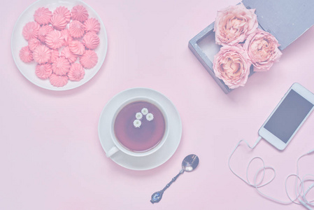 工作空间与智能手机，一杯热凉茶花和棉花糖在粉红色的桌子上。 女性办公桌的创造力。 仍然生活的粉红色项目与粘贴口音。 上面的风景。