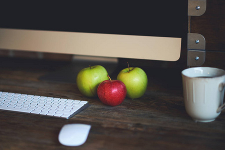 舒适的工作场所与大电脑屏幕鼠标和键盘。 木制桌子，用铅笔画画和五颜六色的苹果。 桌面上有一杯咖啡和新鲜苹果作为健康早餐。