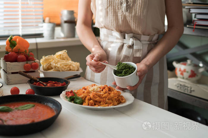 厨房里的年轻女人在家里用平底锅做美味的意大利面和酱汁。 意大利农村烹饪还活着。 木板新鲜蔬菜煮熟的意大利面和一锅酱汁放在木制厨房