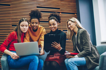积极的年轻多种族女性在笔记本电脑上观看视频，同时与女学生项目组合作，计划工作，并集思广益，利用技术解决问题。