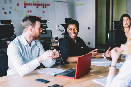 多元文化办公室员工正式穿着,在讨论设计项目时玩得开心,坐在会议桌上