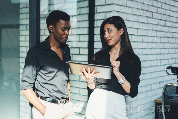 年轻女性与非裔美国人同事交谈,并在现代平板电脑网站上展示视频演示