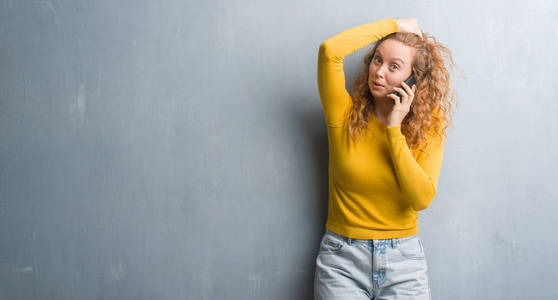 年轻的红头发女人在灰色的墙壁上交谈，在电话上强调，用手在头上震惊，羞愧和惊讶的脸，愤怒和沮丧。 因为错误而恐惧和不安。