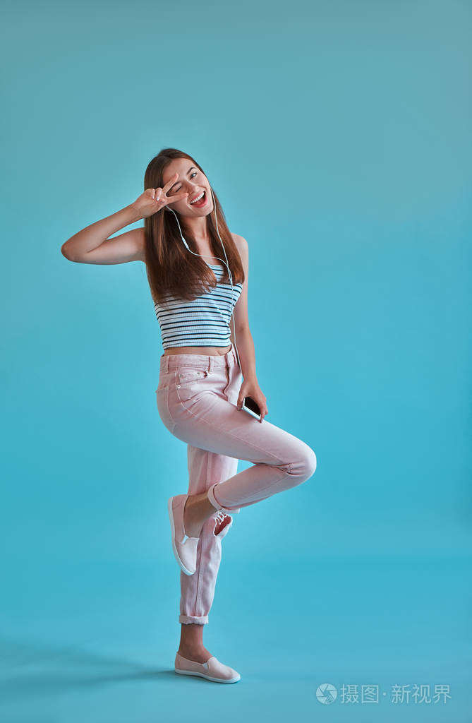 快乐的女孩正在用智能手机和耳机摆姿势.