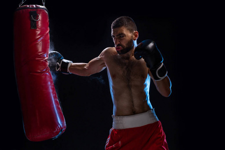 胡子男性拳击手训练与冲压袋在黑色背景。男性拳击手作为运动为大战斗
