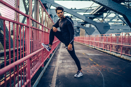 英俊的黑发跑步者穿着黑色运动服装,在训练中休息,同时用耳机听音乐.