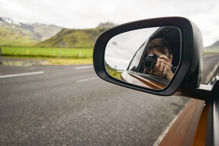 男人在后视镜里拍照，他身后的景色。 公路旅行概念。
