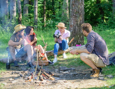 游客徒步坐在原木上放松等待野餐小吃。公司有远足野餐的自然背景。和朋友在篝火旁的森林里野餐。远足者在小吃时间放松。夏季野餐