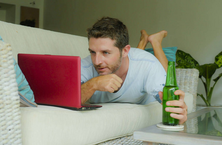 家庭生活方式室内照片年轻有魅力和快乐的男人躺在家里沙发上放松使用互联网笔记本电脑观看在线电影或作为独立自由职业者工作