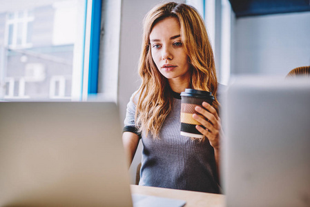 集中女性IT专业更新笔记本电脑上的杀毒软件，使用wifi连接，在同事空间，严肃的时髦女孩在网上看视频，拿着一杯外卖咖啡