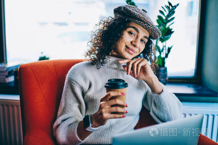 正面女性软件开发商的肖像，享受外卖咖啡和良好的wifi连接上网本快乐微笑的女人穿着时尚的服装，花时间在室内与现代技术。