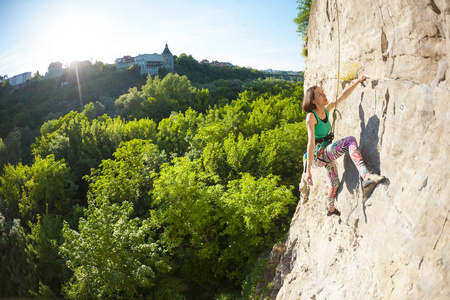女孩在美丽的森林景观的背景下爬上岩石。 女人在大自然中从事健身活动。 极限运动。 在自然地形上攀爬路线。 耐力训练。 锻炼。