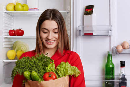 幸福的女人的肖像，有着欢快的表情，手里拿着一个纸袋，里面放着西红柿葫芦笋和生菜，来自去做蔬菜沙拉的商店。 人与健康饮食观念