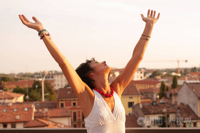 快乐的同时举起双手向天空自由的姿态. 日落时的太阳在城市上.