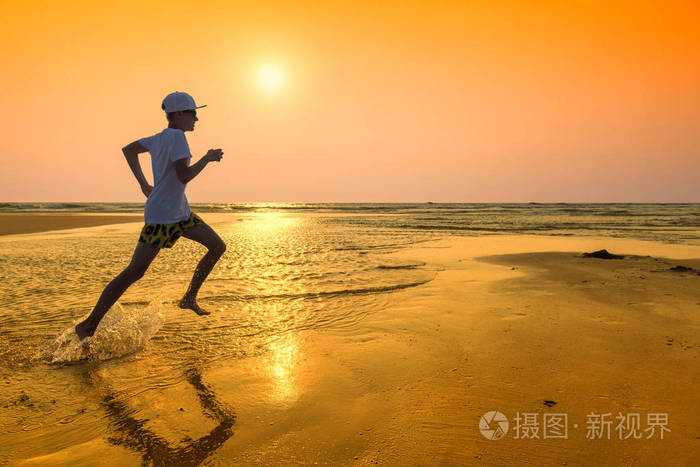 日落时快乐的少年男孩在海滩上奔跑暑假概念
