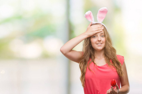 年轻的金发女人戴着复活节兔子耳朵，用手压在头上，羞愧和惊讶的脸，愤怒和沮丧。 因为错误而恐惧和不安。