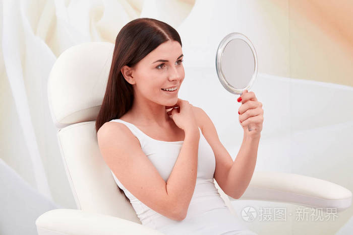 在一家专业的美容诊所里一位年轻女士照镜子看着她的脸