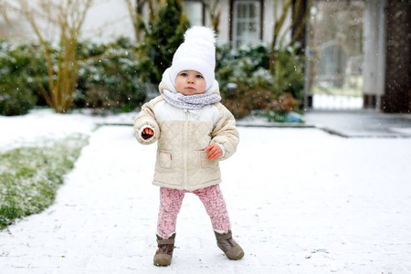 可爱的小女孩, 在冬天做第一步户外活动。可爱的学步孩子学习走路。孩子在寒冷的雪天玩得开心。穿着温暖的婴儿粉红色的衣服和帽子与 b