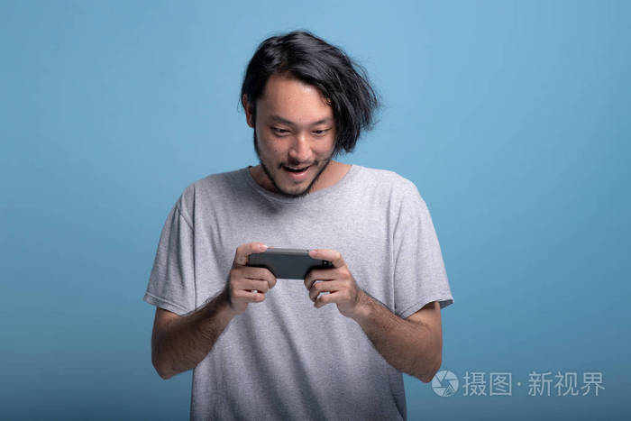 兴奋的小胡子男人在蓝色背景下玩手机游戏.