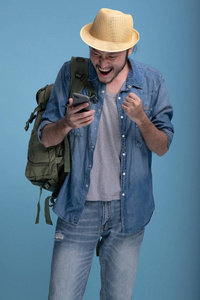 带着蓝色背景的年轻留胡子的人背包旅行。 非常高兴的亚洲年轻臀部使用手机找到一个位置半身体射击。 年轻一代嬉皮士度假旅游理念。