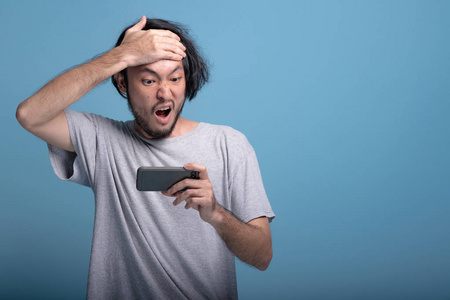 心烦意乱的小胡子男人在蓝色背景下玩手机游戏.