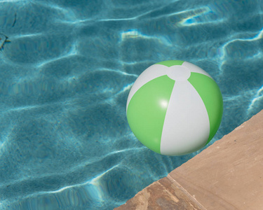 靠近顶部视图，一个明亮的绿色海滩球附近的池应对边缘。 漂浮在清爽的蓝色水中，波浪在池甲板和瓷砖附近的夏季阳光下反射。 儿
