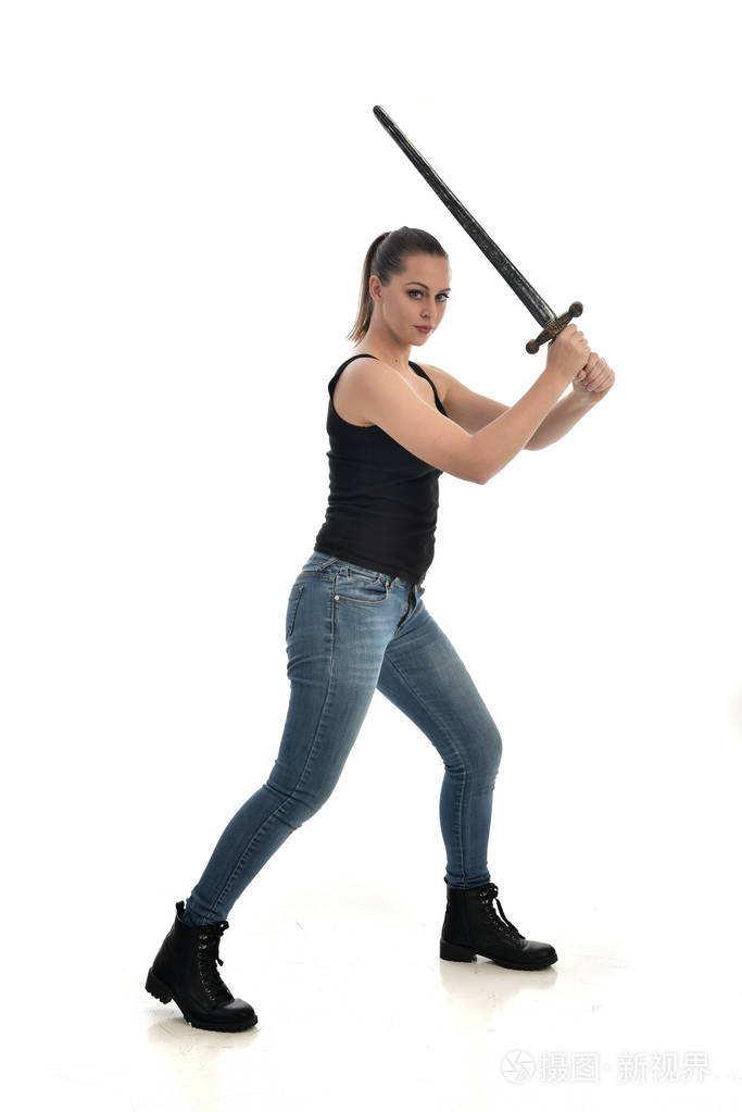 穿黑色单身牛仔裤的黑发女孩的全长肖像站着摆姿势拿着剑孤立在白色