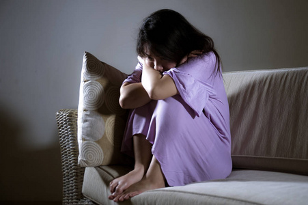年轻的悲伤和沮丧的亚洲妇女在家沙发沙发上哭泣,绝望和无助,痛苦