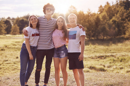 亲密朋友的照片站在户外野餐,一起拥抱和微笑,在镜头前愉快地有着良好