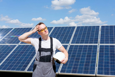太阳能电池板工程师，戴着保护黄色眼镜和灰色工作服，手里拿着白色的木桶，在太阳能电池板领域附近工作。 炎热晴朗的夏天天气。 可再生