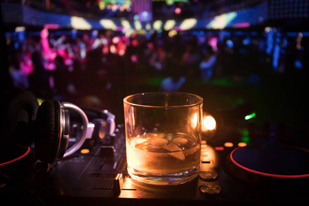 在夜总会的dj控制器里装有冰块的威士忌玻璃。Dj控制台与俱乐部饮料在夜总会的音乐聚会与迪斯科灯。选择性重点