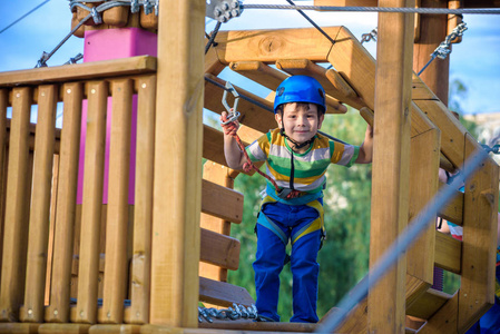 小可爱的男孩在夏天阳光明媚的日子里在攀岩冒险公园里享受活动。 蹒跚学步的孩子在绳索操场结构中攀爬。 安全攀登极限运动与头盔和卡宾