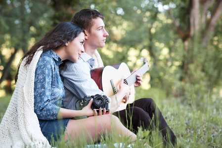年轻夫妇坐在森林里弹吉他，夏天的大自然，明亮的阳光，阴影和绿叶，浪漫的感情