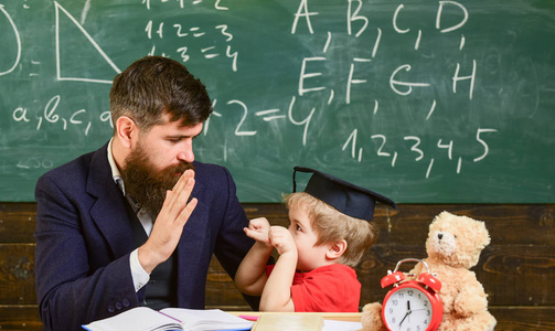 孩子在学习时开朗分心, 注意力不足。顽皮的孩子概念。老师和学生在 mortarboard, 黑板在背景。父亲有胡子, 老师教儿子