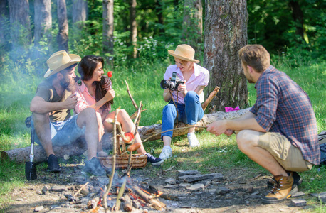 公司有远足野餐的自然背景。和朋友在篝火旁的森林里野餐。徒步旅行者分享漫步森林的印象。夏天的传统。游客分享徒步旅行的想法坐在日志上