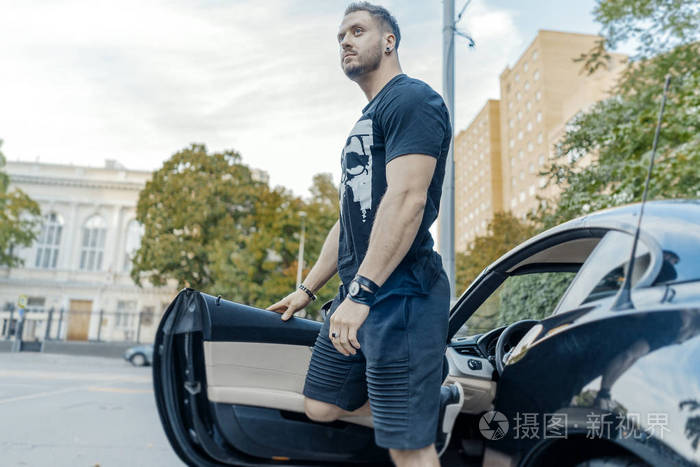 关闭的年轻迷人的男子下车的黑色汽车侧面视图