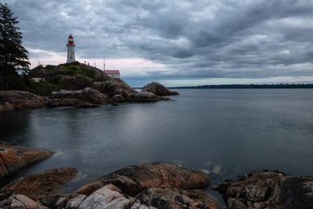 灯塔在岩石海岸，在一个充满活力的多云日落。 取自加拿大不列颠哥伦比亚省温哥华西部马蹄湾。