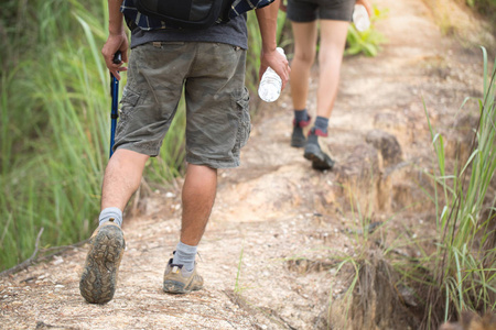 一个女人和一个男人在山林中走一条路。 从后面看。 双腿穿着运动鞋靠近。 徒步旅行鞋。