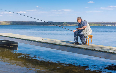 准备好钓鱼老渔夫坐在码头上拿着鱼竿,准备钓鱼照片