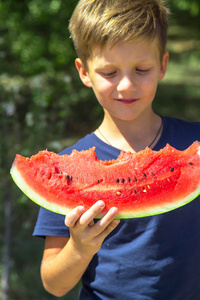 白种人男孩抱着吃了一大片红色成熟西瓜。 夏秋季节。 健康的生食和维生素概念