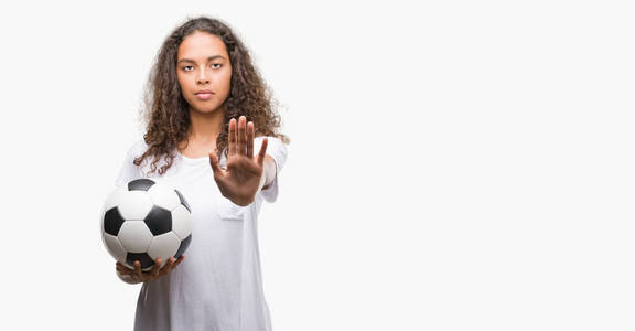 年轻的西班牙裔女子，用张开的手拿着足球球，用严肃而自信的表情做停牌，做防守手势