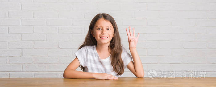 年轻的西班牙裔孩子坐在家里的桌子上，用手指第四，一边微笑，自信和快乐。