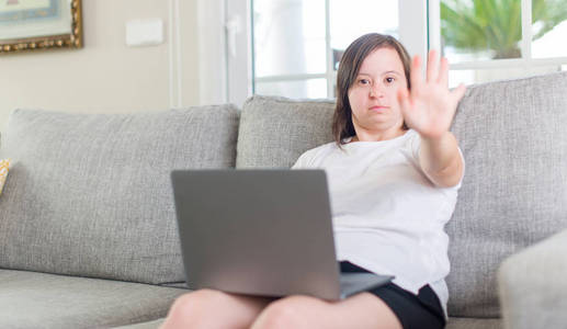 唐氏综合征妇女在家使用电脑手提电脑，手张开，表情严肃自信，做手势