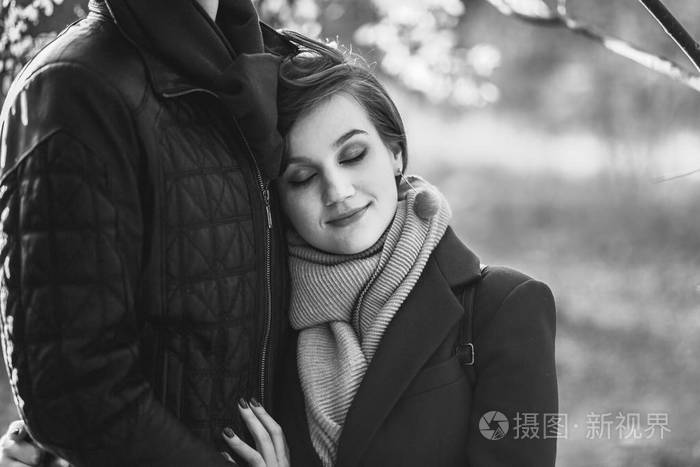 年轻美丽的女人的肖像,闭着眼睛靠在男人身上,穿着便服,拥抱在秋天的