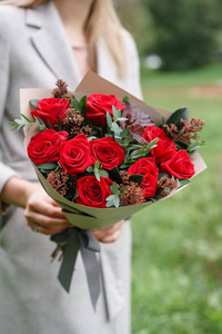 可爱的女人捧着美丽的秋花束。花安排与康乃馨和红色庭院玫瑰。颜色粉红色。背景绿色草坪